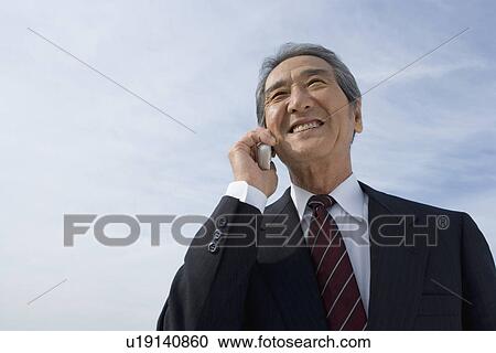 Stock Image - A Senior Adult Man Smiling and Talking on a Mobile Phone Under the Sky, Low Angle View, Copy Space. Fotosearch