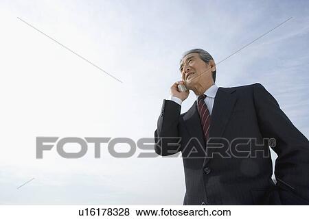 A Senior Adult Man Smiling and Talking on a Mobile Phone Under the Sky, Low Angle View, Copy Space View Large Photo Image Stock Photo - A Senior Adult Man Smiling and Talking on a Mobile Phone Under the Sky, Low Angle View, Copy Space. Fotosearch