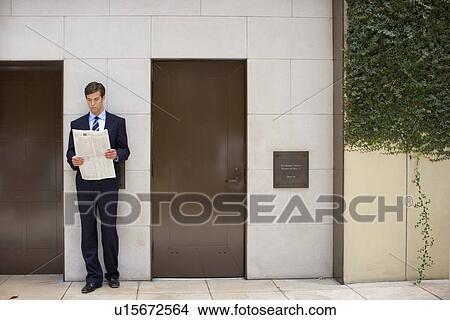 Picture - A Young Adult Businessman Standing by the Building and Reading a Newspaper, Front View, Full Length. Fotosearch