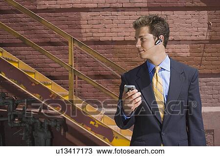 Stock Image - A Young Adult Businessman Using a Headset Cellular Phone, Front View, Waist Up. Fotosearch