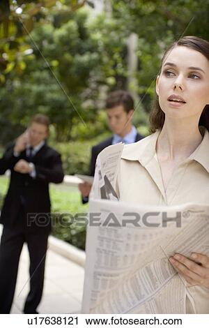 Stock Image - A Young Adult Businesswoman Holding a Newspaper and Looking Away, Head and Shoulders, Differential Focus. Fotosearch