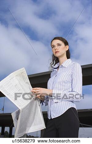 Stock Photo - A Young Adult Businesswoman Holding a Newspaper and Looking Away, Three Quarter Length, Low Angle View. Fotosearch