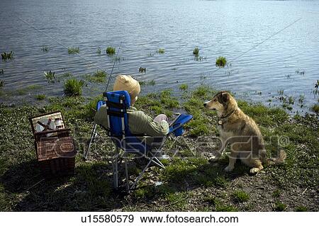 Stock Photo - Boy (12-14) fishing by river with pet dog, rear view. Fotosearch