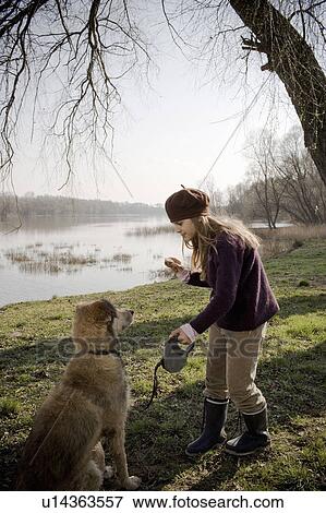 Stock Photo - Girl (10-12) standing by river holding piece of cake in front of dog. Fotosearch