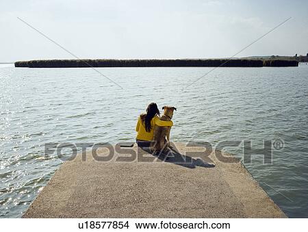 Girl sitting with dog by lake rear view. View Large Photo Image Picture - Girl sitting with dog by lake rear view.. Fotosearch