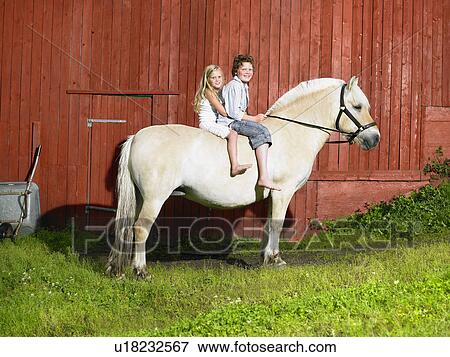 Young boy and young girl smiling on a horse in front of a red wall. View Large Photo Image Stock Photo - Young boy and young girl smiling on a horse in front of a red wall.. Fotosearch