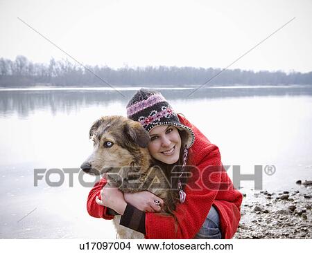 Picture - Young woman kneeling by river embracing dog, smiling, portrait. Fotosearch