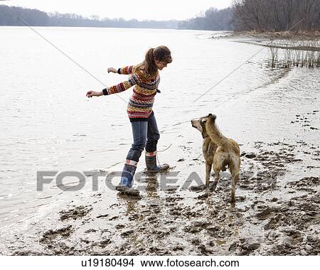 Picture - Young woman playing with dog by river. Fotosearch