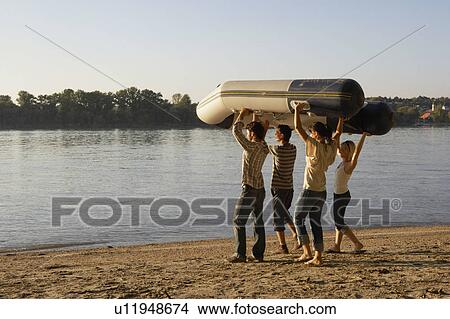 Four friends carrying a raft on a beach. View Large Photo Image Picture - Four friends carrying a raft on a beach.. Fotosearch