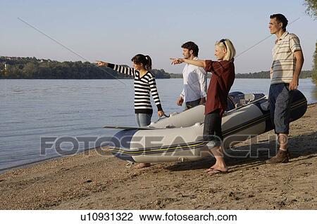 Stock Image - Four friends with a raft on a beach smiling and pointing.. Fotosearch