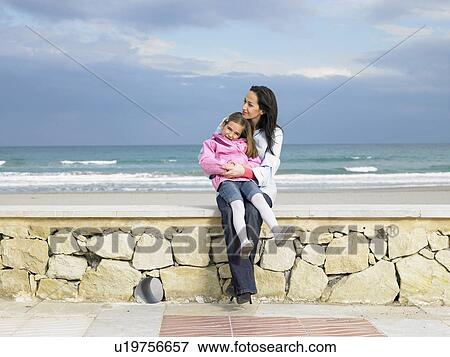 Mother and daughter (6-8) sitting on wall by beach View Large Photo Image Stock Photo - Mother and daughter (6-8) sitting on wall by beach. Fotosearch