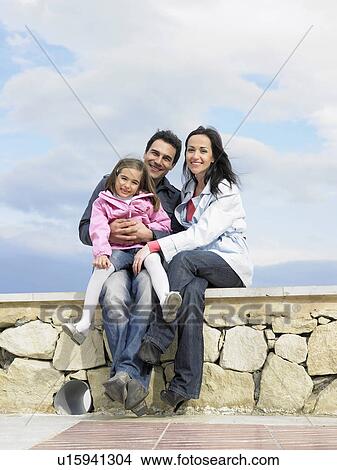 Parents and daughter (6-8) sitting on wall, smiling, portrait View Large Photo Image Picture - Parents and daughter (6-8) sitting on wall, smiling, portrait. Fotosearch