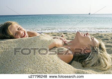 Woman buried in sand at the beach with young girl leaning on her and laughing. View Large Photo Image Stock Photo - Woman buried in sand at the beach with young girl leaning on her and laughing.. Fotosearch
