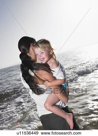 Woman holding a smiling young girl at the beach. View Large Photo Image Stock Photo - Woman holding a smiling young girl at the beach.. Fotosearch