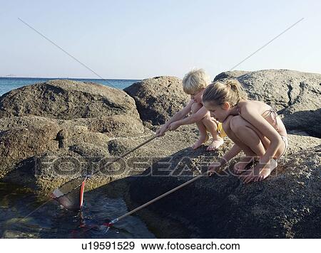 Young boy and young girl crouched on rocks fishing with nets. View Large Photo Image Stock Photo - Young boy and young girl crouched on rocks fishing with nets.. Fotosearch