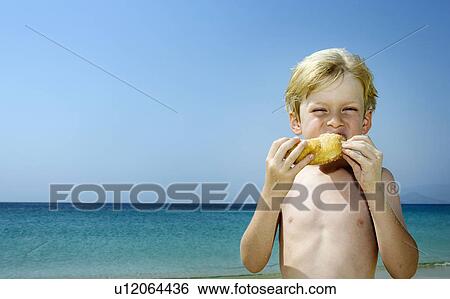 Stock Photograph - Young boy eating a doughnut at the beach.. Fotosearch