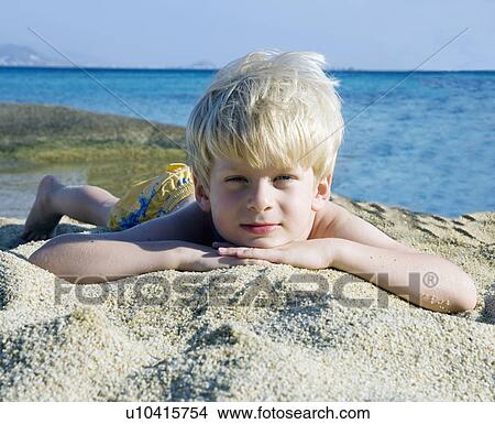 Young boy lying in the sand at the beach. View Large Photo Image Picture - Young boy lying in the sand at the beach.. Fotosearch