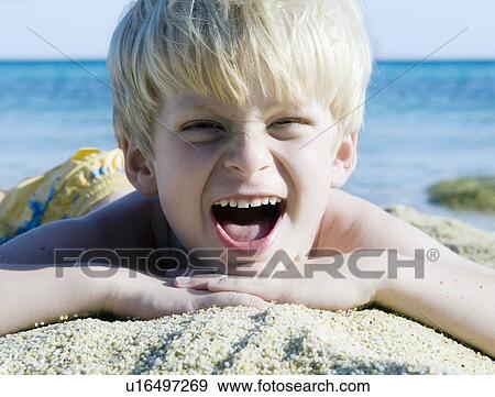 Stock Photo - Young boy lying in the sand at the beach yelling.. Fotosearch