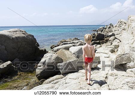 Young boy walking on rocks near the water. View Large Photo Image Stock Image - Young boy walking on rocks near the water.. Fotosearch