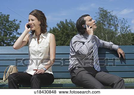Stock Photo - Businessman and women talking on cell phones while sitting on bench outside.. Fotosearch