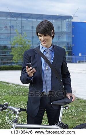 Businessman holding bike and looking at cell phone. View Large Photo Image Stock Photograph - Businessman holding bike and looking at cell phone.. Fotosearch