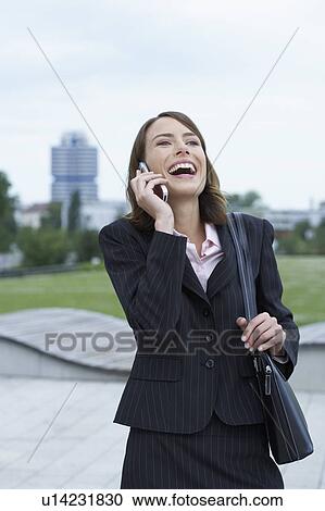 Stock Image - Businesswoman on the mobile big smile city and park in background.. Fotosearch