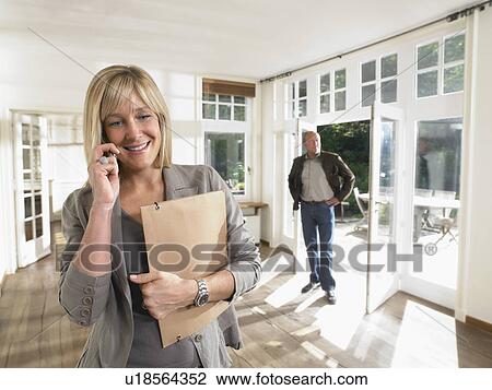 Female real estate agent on phone in show house male client in background. View Large Photo Image Stock Image - Female real estate agent on phone in show house male client in background.. Fotosearch