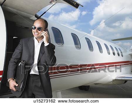 Stock Image - Smiling businessman exiting private jet on phone.. Fotosearch
