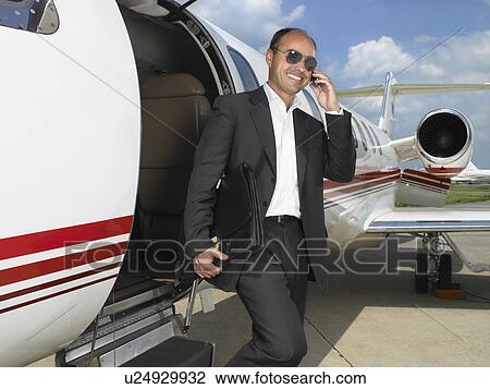Stock Image - Smiling businessman exiting private jet while on phone.. Fotosearch