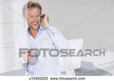 Stock Image - Smiling man in office on phone.. Fotosearch