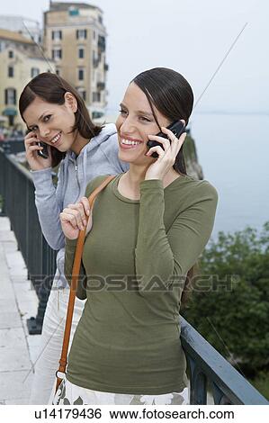Stock Photograph - Two young girls both on the mobile smiling old city in background.. Fotosearch