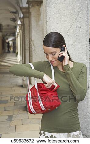 Young woman leaned at wall of ambulatories on the mobile fishing something out of her handbag smiling. View Large Photo Image Stock Image - Young woman leaned at wall of ambulatories on the mobile fishing something out of her handbag smiling.. Fotosearch