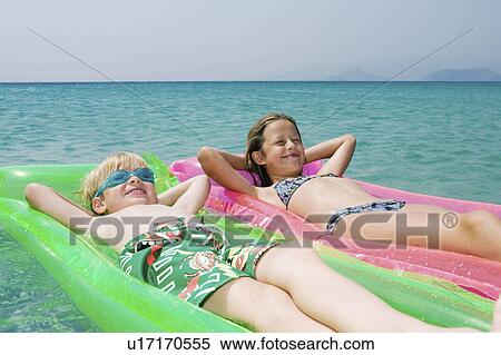 Stock Photography - Young boy and young girl floating on inflatable rafts in the water smiling.. Fotosearch