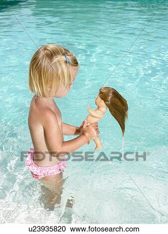 Stock Image - Young boy playing with a doll in a pool.. Fotosearch