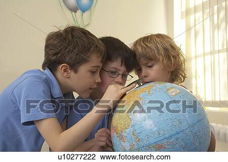Stock Image - Boys looking at an earth globe. Fotosearch