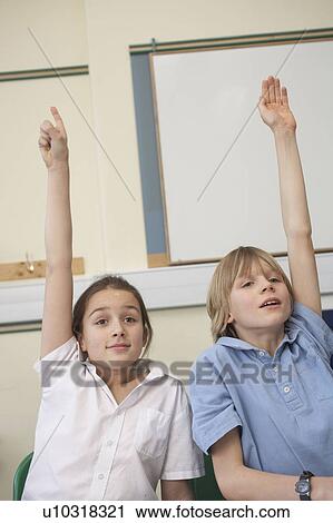 Stock Image - Children raising hands in classroom. Fotosearch