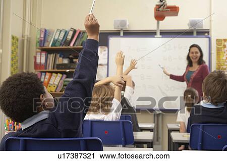 Stock Image - Children raising hands in classroom. Fotosearch
