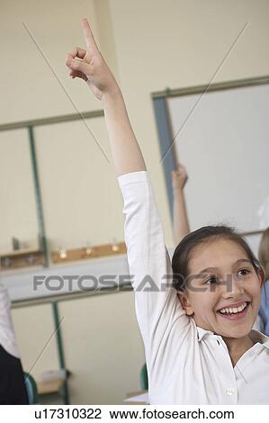 Stock Image - Girl raising her hand in classroom. Fotosearch