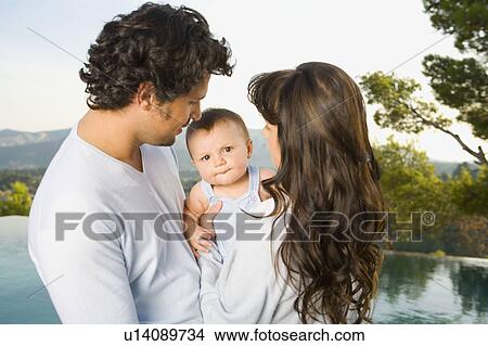 Couple holding a baby by an infinity pool outdoors. View Large Photo Image Picture - Couple holding a baby by an infinity pool outdoors.. Fotosearch