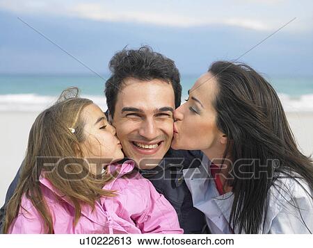 Stock Image - Mother and daughter (6-8) kissing father from each side at beach. Alicante, Spain.. Fotosearch