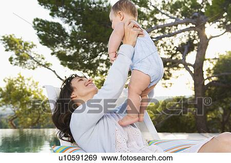 Woman holding a baby by an infinity pool smiling. View Large Photo Image Stock Photo - Woman holding a baby by an infinity pool smiling.. Fotosearch