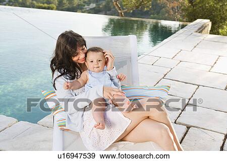Woman holding a baby by an infinity pool smiling. View Large Photo Image Stock Photo - Woman holding a baby by an infinity pool smiling.. Fotosearch