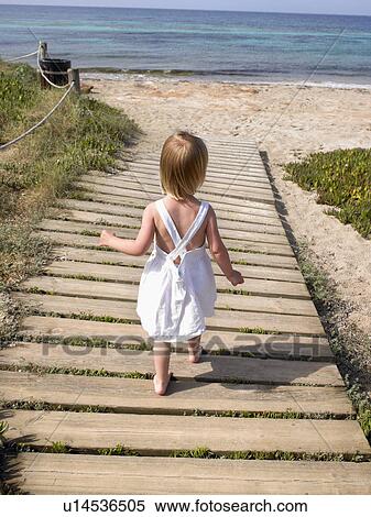 Stock Photography - Young boy walking on a wooden path at the beach.. Fotosearch