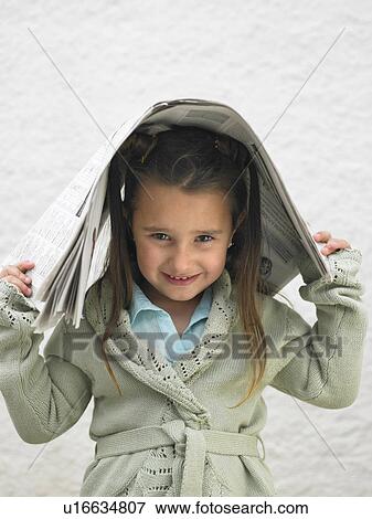 Stock Photo - Young girl (4-6) holding a newspaper over head, portrait. Fotosearch