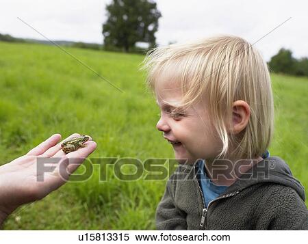 Stock Photography - Young girl smiling looking at a small frog held in a man's hand.. Fotosearch