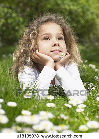 Stock Photo - Young girl with flower in mouth lying in the grass.. Fotosearch