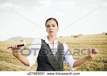 Stock Image - Businesswoman fencing in a wheat field.. Fotosearch