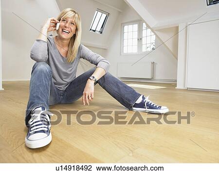 Happy woman seated on wooden floor giving a call with her cellular. White empty loft. View Large Photo Image Stock Image - Happy woman seated on wooden floor giving a call with her cellular. White empty loft.. Fotosearch