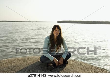 Stock Image - Woman sitting by a lake.. Fotosearch