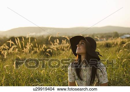 Picture - Woman wearing hat sitting in grass.. Fotosearch